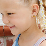 Young girl wearing a blue and white striped sweater, crayon box earrings with a backpack, standing against a brick wall.