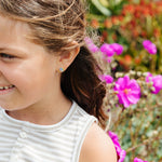 Young girl with a striped shirt standing in front of pink flowers with planet earrings