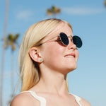 Girl wearing sunglasses with a clear blue sky and palm trees in the background earth earrings