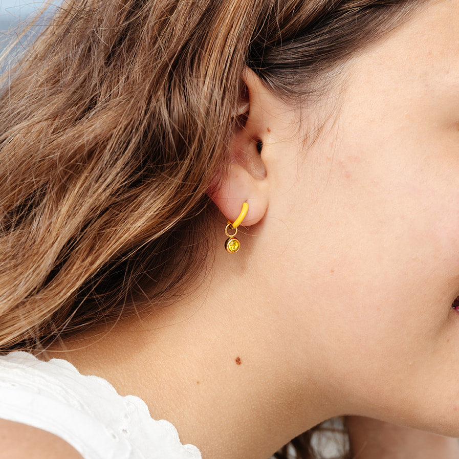 Close-up of a person wearing a yellow birthstone earring with a white sleeve.
