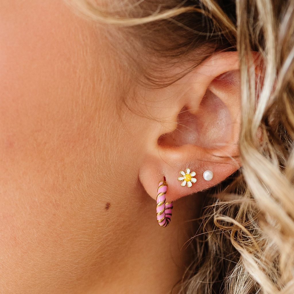 Close-up of an ear with pink candy-shaped earrings and a small white flower earring.
