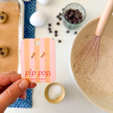 Hand holding a 'pip pop' card with baking ingredients and tools in the background