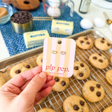 Hand holding a 'pip pop' product card with cookies and baking ingredients in the background
