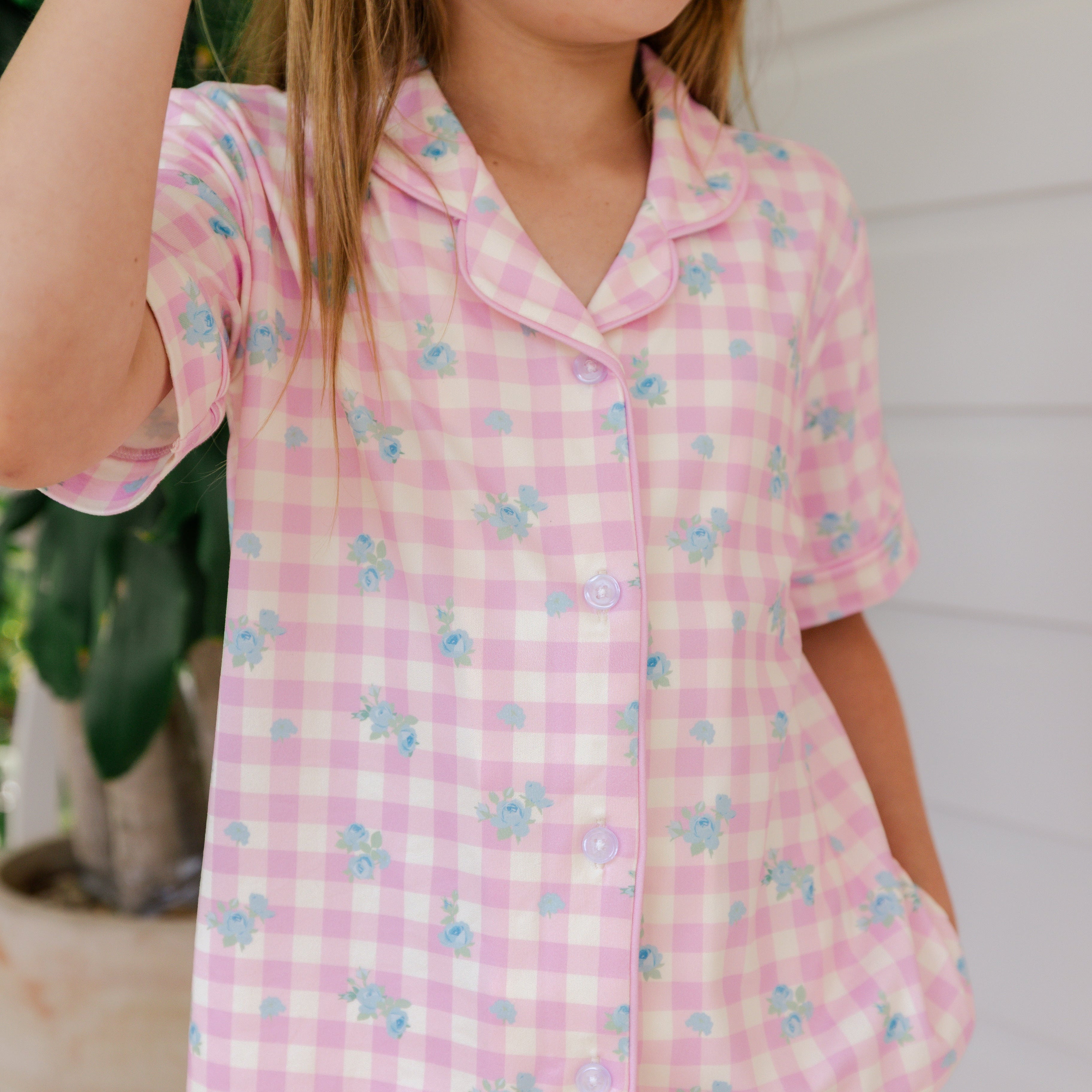Child wearing a pink checkered outfit with floral patterns outdoors.