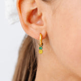 Gold hoop earring with a pineapple charm worn by a person.