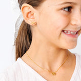 Close-up of a young girl wearing gold bow earrings and a  gold bow necklace on a white background