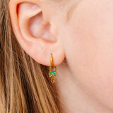 Gold hoop earring with a palm tree design worn by a person with blonde hair.