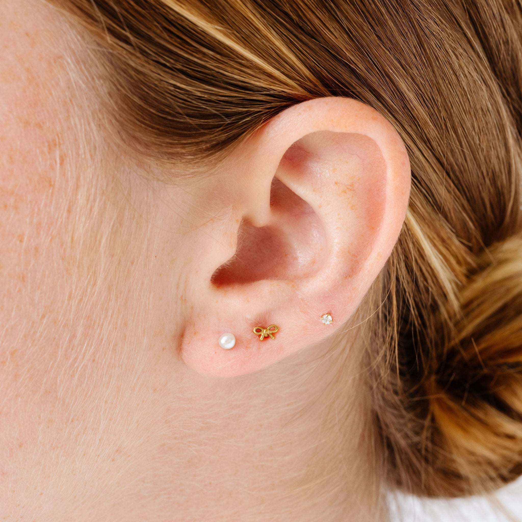 Close-up of an ear with pearl, bow and diamond stud earrings.