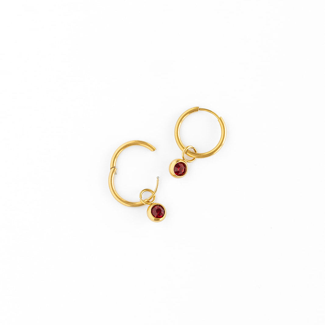 Gold hoop earrings with red birthstones on a white background