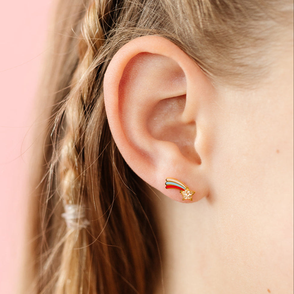 close up of ear wearing Gold earrings with rainbow shooting star
