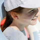 Girl wearing a sailboat stud earring smiling with white hat on