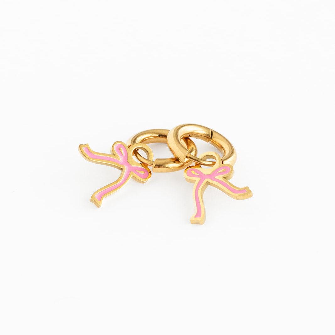 Gold hoop earrings with pink bow charm on a white background
