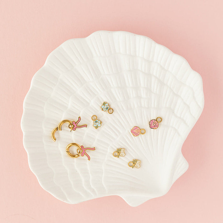 Set of earrings displayed on a white shell against a pink background
