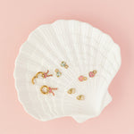 Set of earrings displayed on a white shell against a pink background