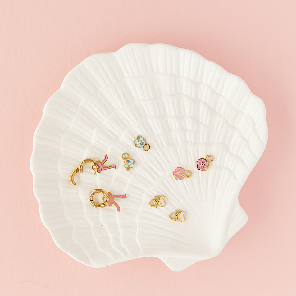 Set of earrings displayed on a white shell against a pink background
