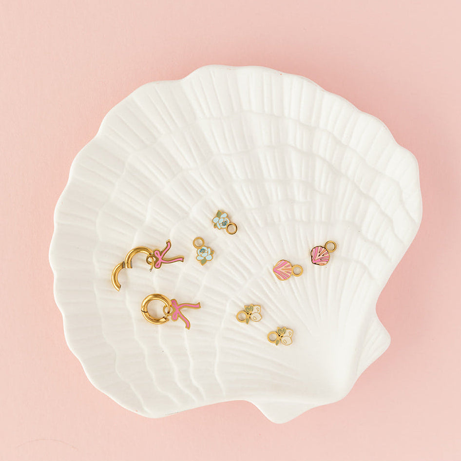 Set of earrings displayed on a white shell against a pink background