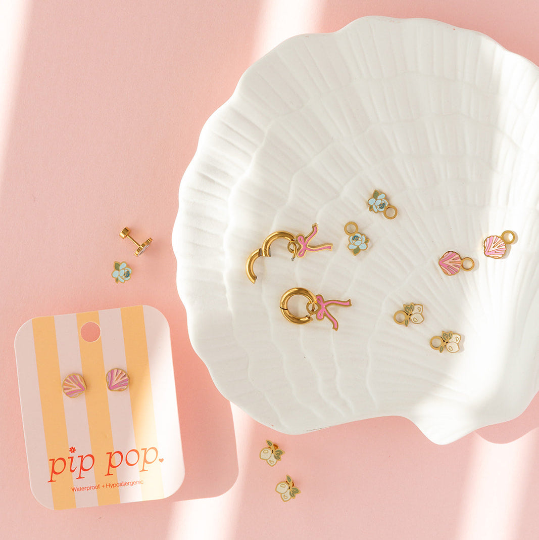Set of gold earrings on a white dish with a pink background