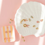 Set of gold earrings on a white dish with a pink background