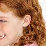 Close-up of a young girl with red hair wearing earrings on a white background
