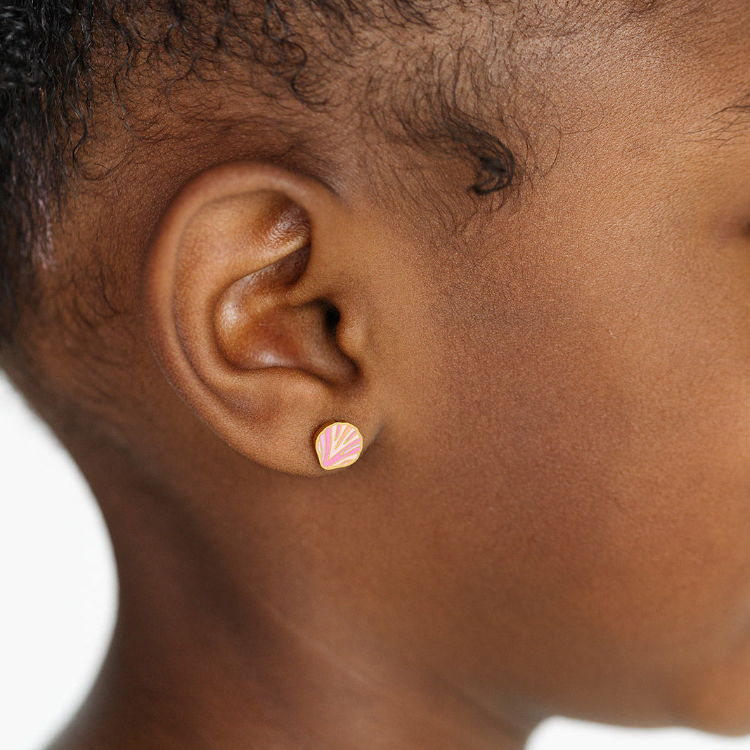 Close-up of an ear wearing a small pink seashell earring on a white background