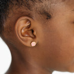Close-up of an ear wearing a small pink seashell earring on a white background