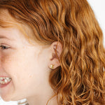 Close-up of a girl with curly hair wearing a gold lemon earring on a white background