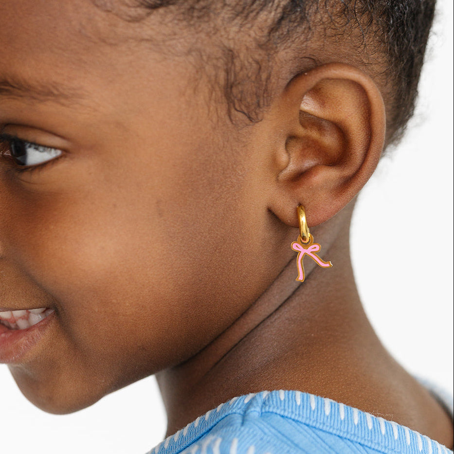 Close-up of a girl wearing a pink bow earring on a white background