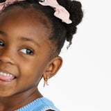 Girl wearing gold hoops with pink bow charms on white background