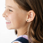 Close-up of a young girl with a backpack, showing her ear with a yin yang earring.